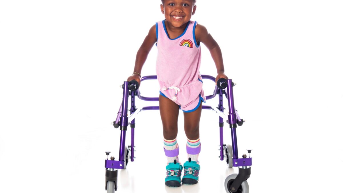 Young girl with cerebral palsy taking steps using her walker, wearing bilateral molded ankle foot orthoses.
