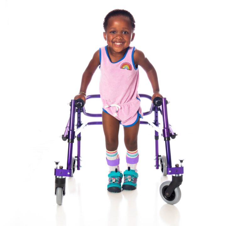 Young girl with cerebral palsy taking steps using her walker, wearing bilateral molded ankle foot orthoses.